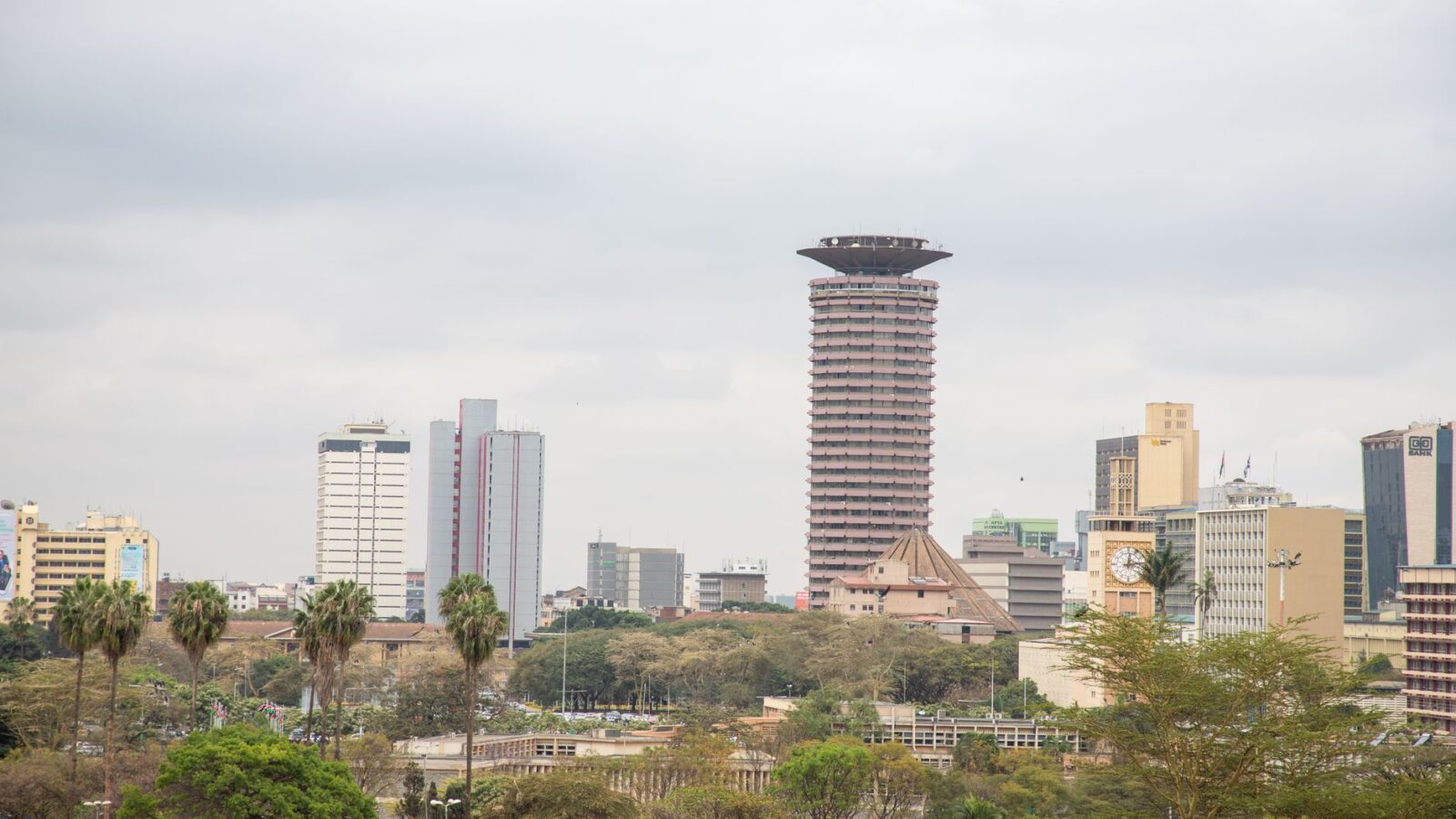 View of Nairobi's skyline with the iconic KICC tower and surrounding high rises under a cloudy sky.