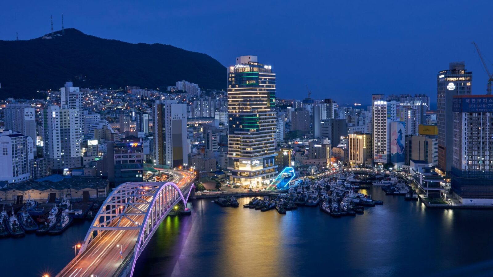 Aerial view of Busan's vibrant cityscape and illuminated bridge at night.