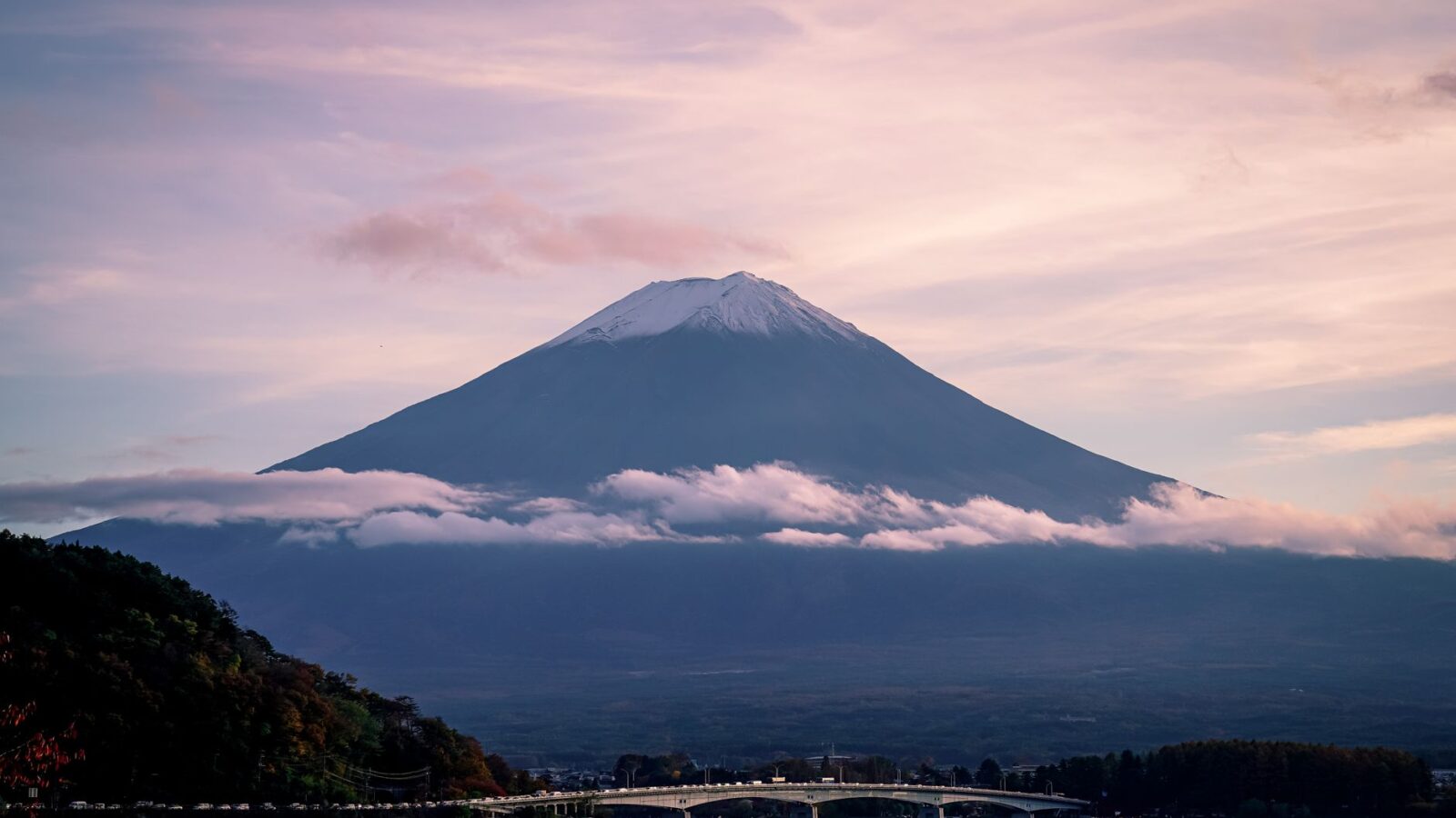 A breathtaking view of Mount Fuji with delicate clouds and serene waters beneath a pastel sky.