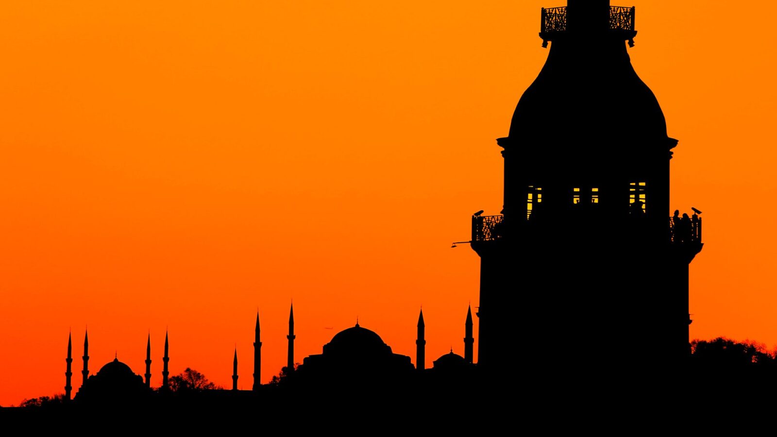 Silhouette of Istanbul's iconic skyline against a vibrant orange sunset.