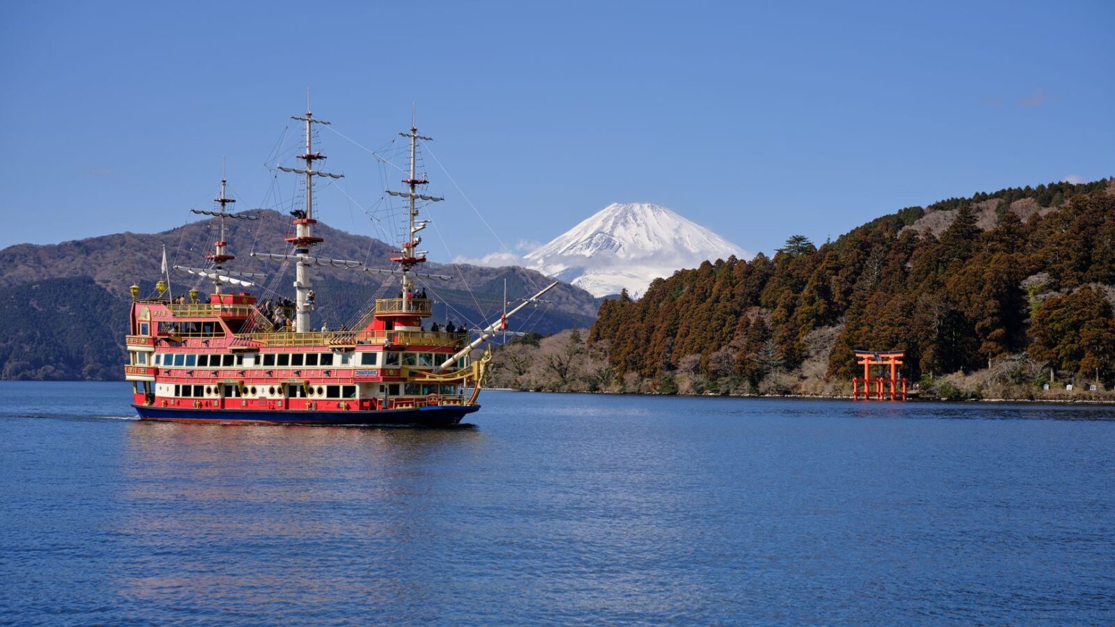 Colorful pirate ship sailing on Lake Ashi with Mount Fuji in the background and a Torii gate along the shore.