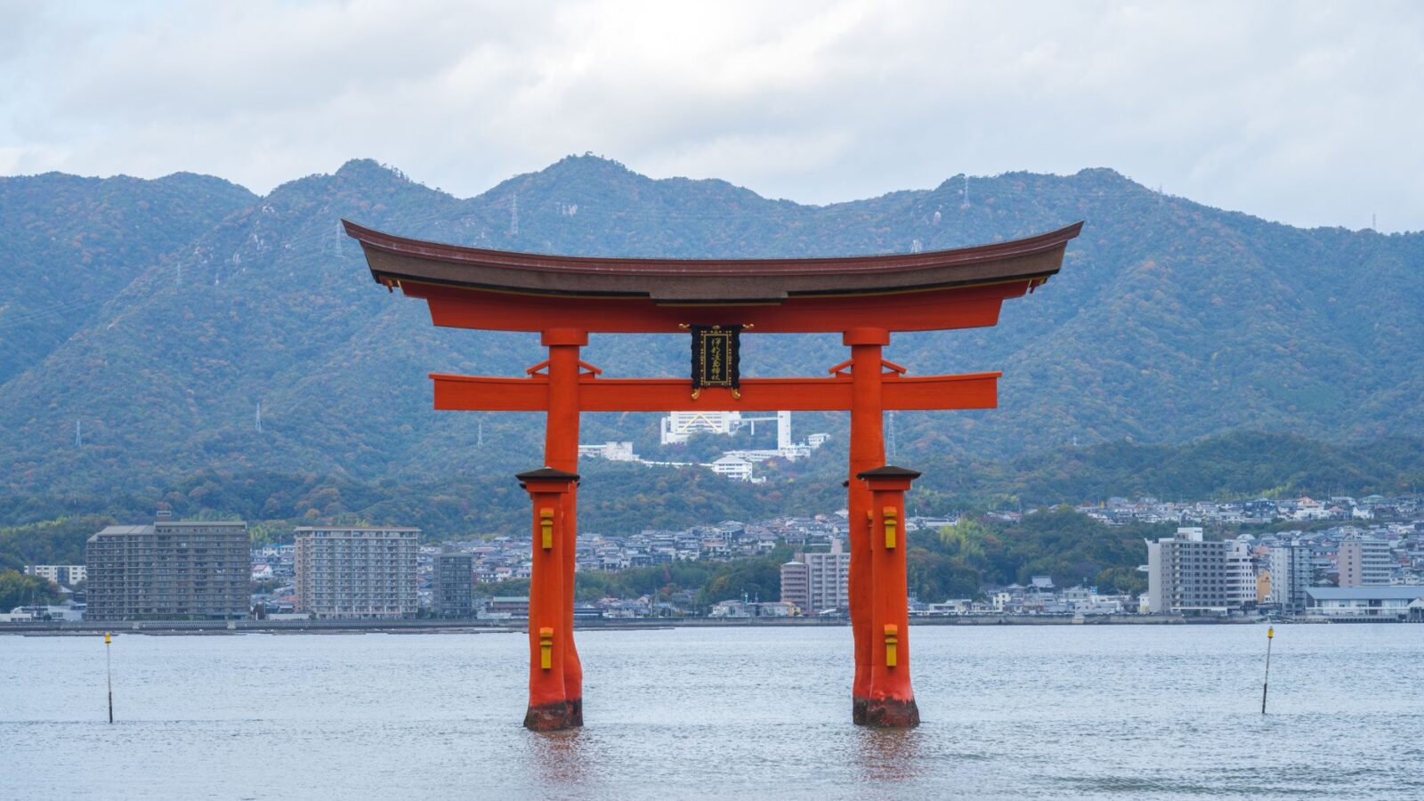 Scenic view of the floating Torii gate at Itsukushima Shrine in Japan, with mountains and sea.