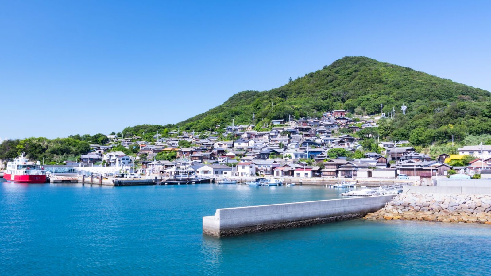 Idyllic Japanese village by the sea with boats, lush greenery, and clear skies.