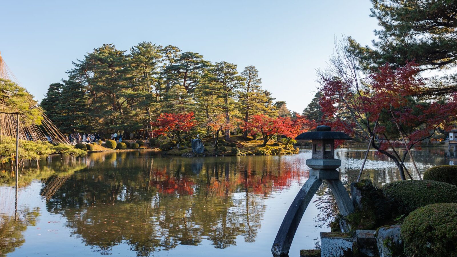 Beautiful autumn landscape at Kenrokuen Garden with vibrant foliage reflected on a tranquil pond.
