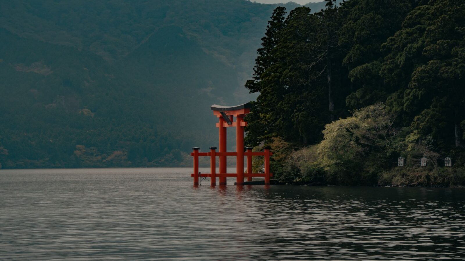 Serene view of the red Torii gate in Lake Ashi, surrounded by lush nature in Hakone, Japan.